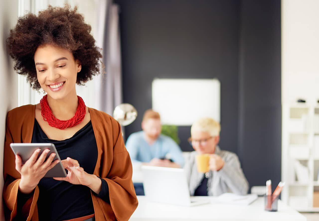 A person working in an office space looks at a tablet while smiling