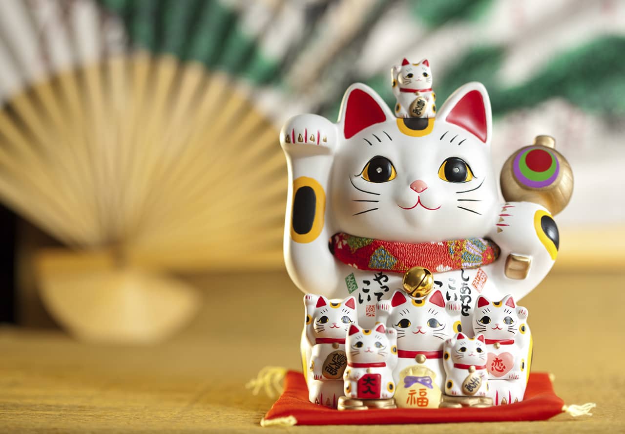 A maneki-neko cat, a white cat with it's right paw raised, with smaller maneki-neko cats