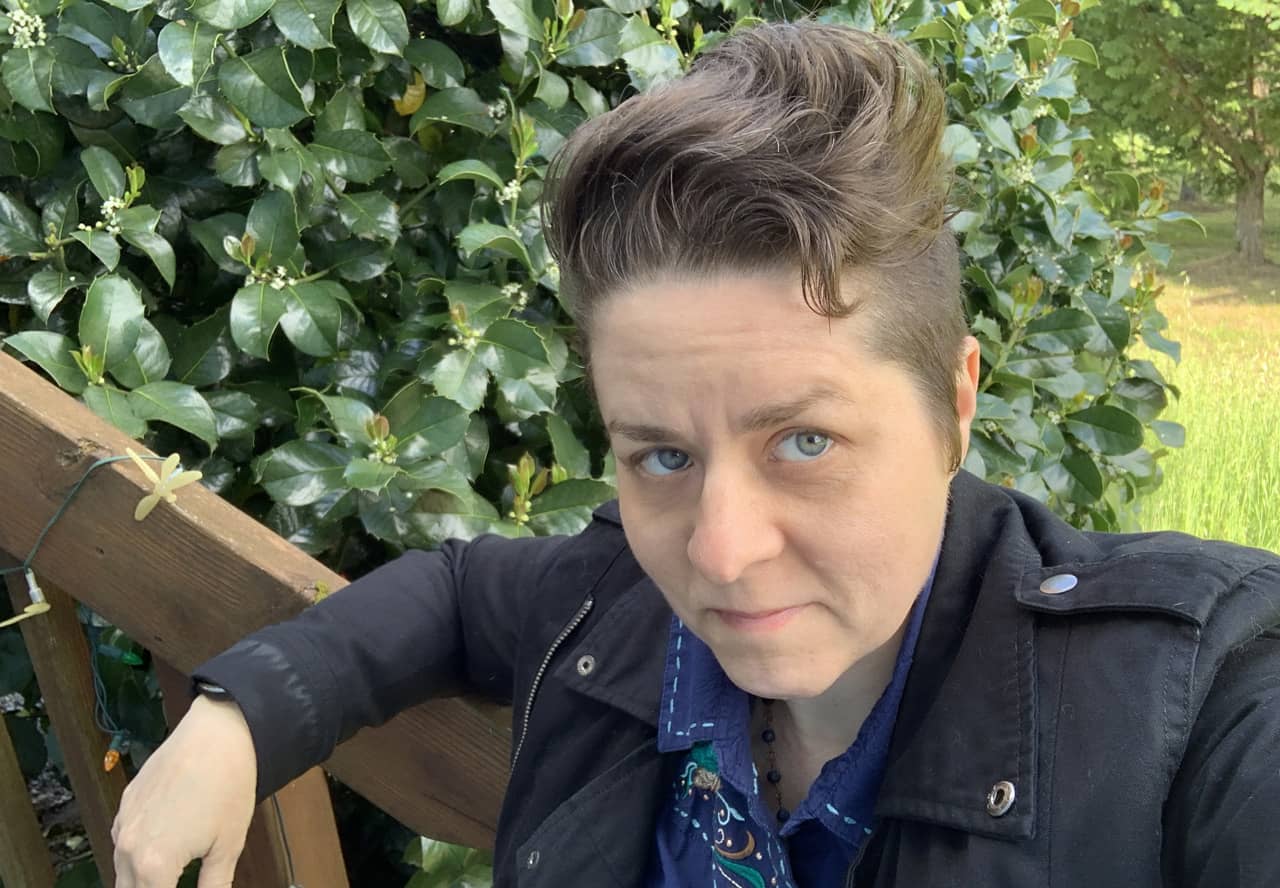 A photo of Sherry Holub leaning on the railing of some wooden steps in front of a large holly bush