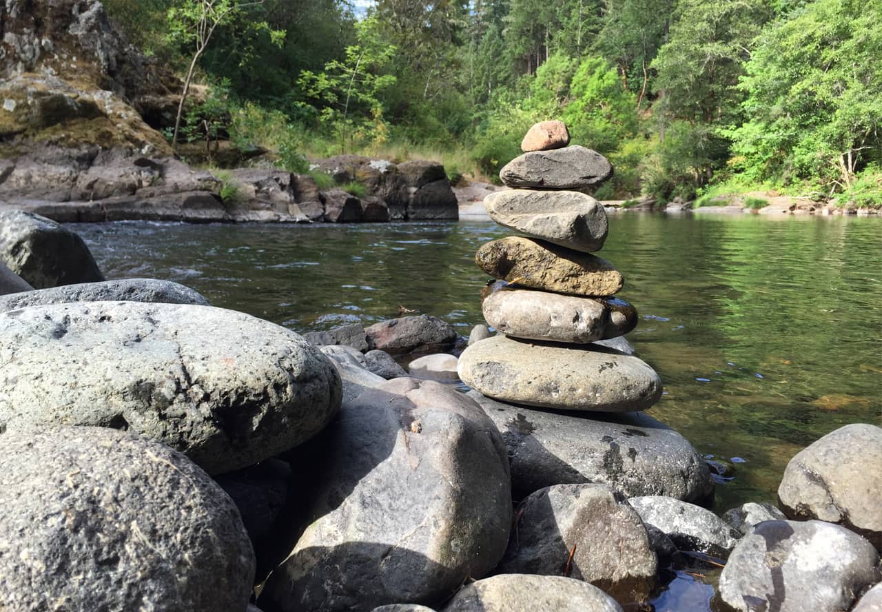 A photo of stacked river rocks in front of a calm river
