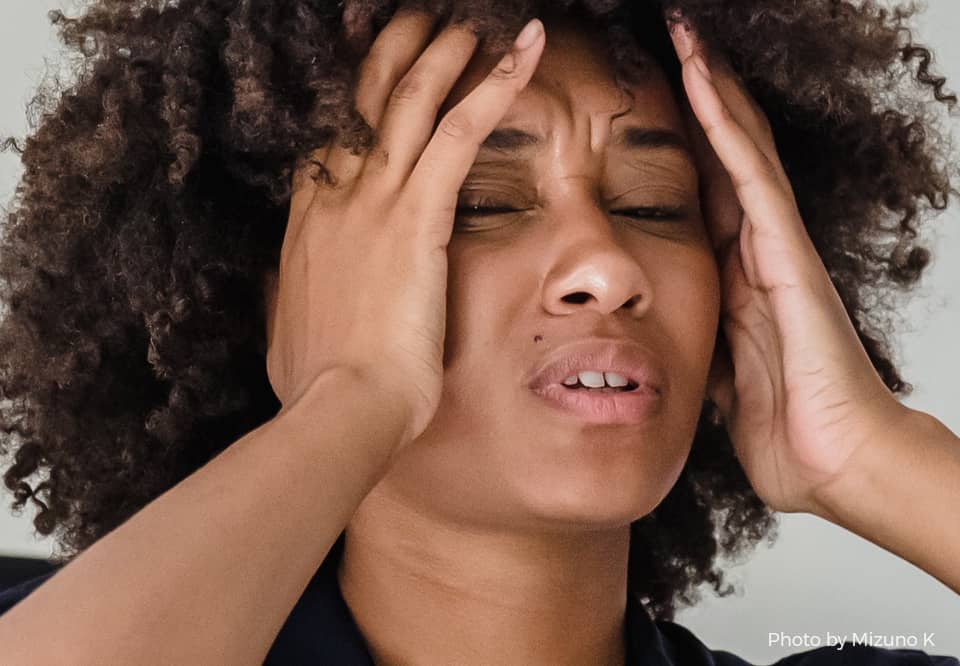 A photo of a person making a face as if experiencing issues and holding their hands against the sides of their head