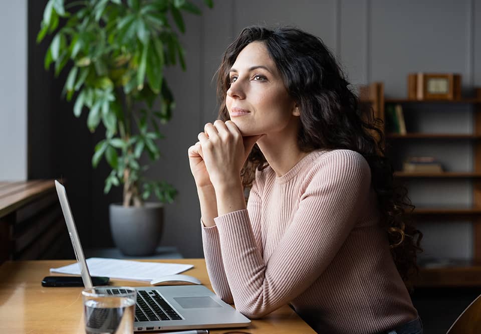 a woman sitting at a desk with open laptop and she is dreaming of her goals