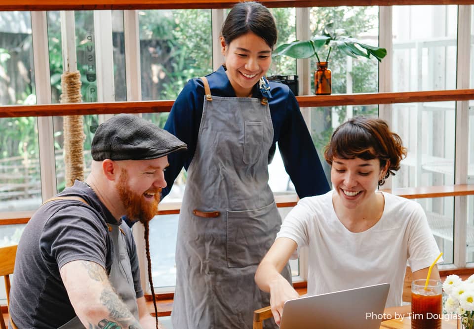 A photo of 3 colleagues looking at a laptop in a cafe