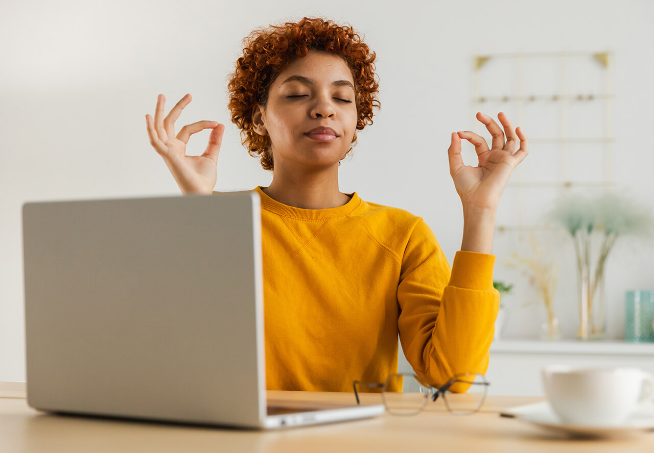 a person in a meditative pose sits in front of a laptop computer